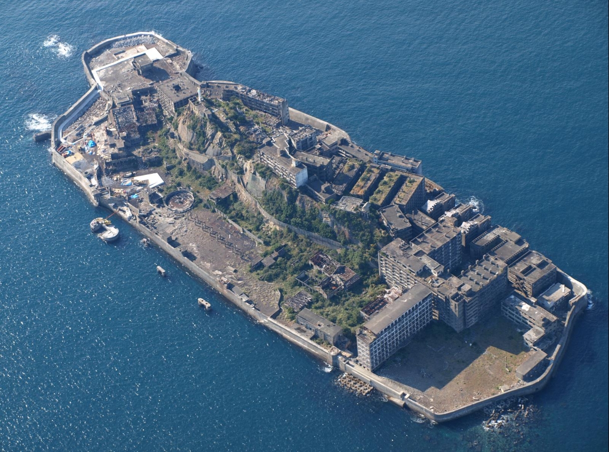 Hashima Island seen from the sea, showing the 'battleship' silhouette of dense concrete buildings on a small island surrounded by seawall.
